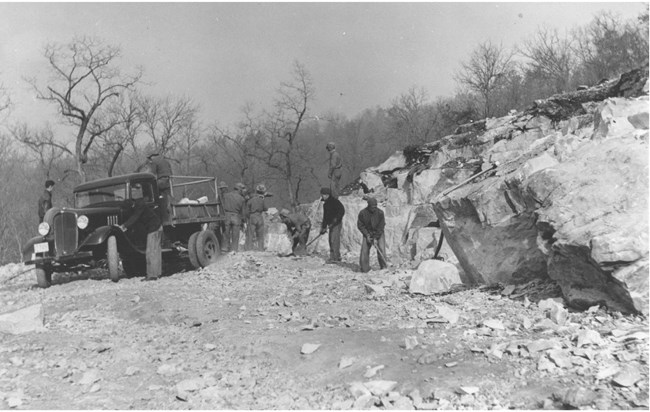 Members of a CCCC crew use shovels to dig stone from a quarry beside a pickup truck