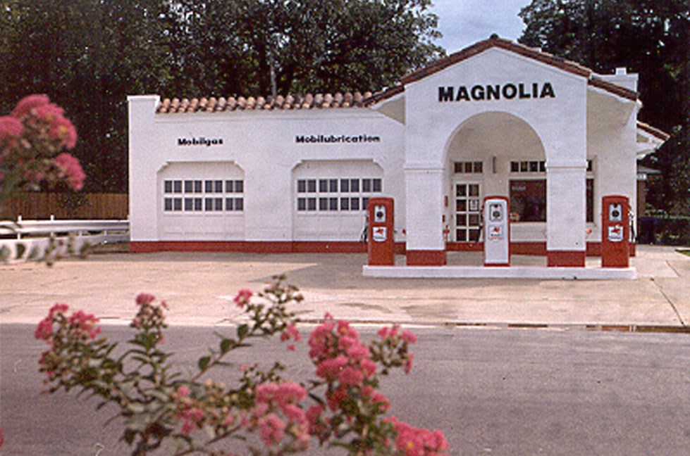 Gas station with several garage doors, three pumps, and a covered entrance that says "Magnolia"