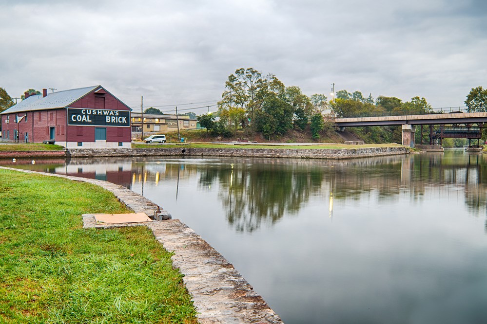 CHOH Cushwa Basin A warehouse with "Cushwa's Coal Brick" painted on the side stands next to a wide basin of water, edged by stone walls and turf.