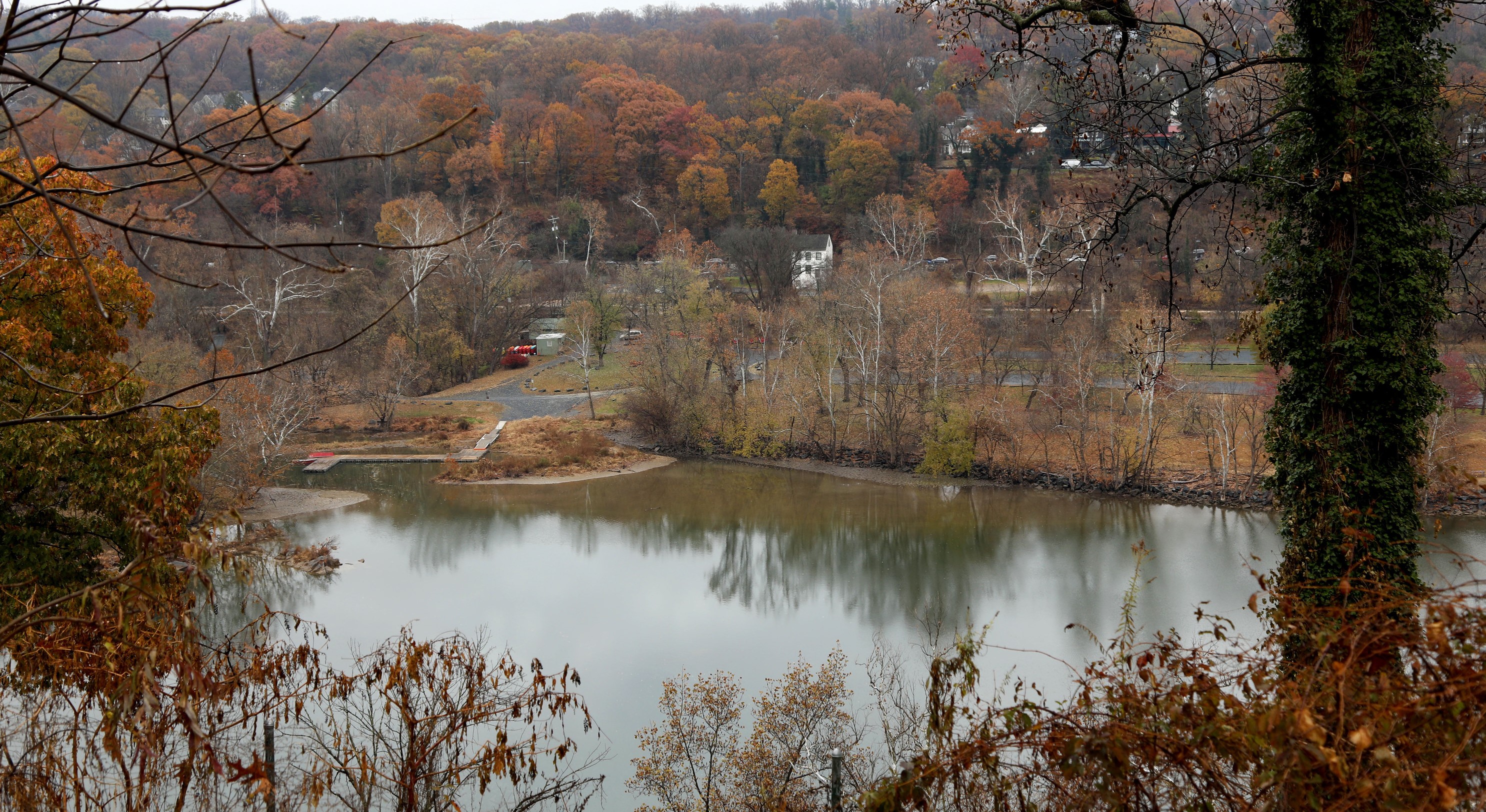 A fall landscape with colorful trees along a river and a boat dock, loop drive and parking lot, and white house along a barely-visible dirt canal towpath.