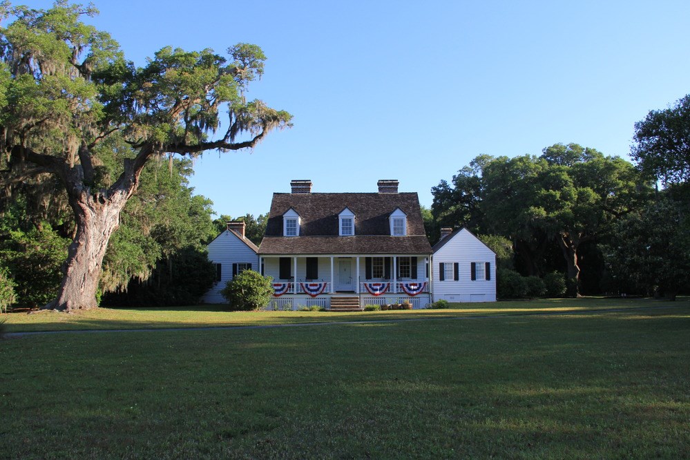 Snee Farm is a two-story white house surrounded by open  lawn and large, leafy trees, with patriotic bunting on the front porch.