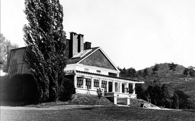 Apple trees in front of Little Studio, c. 1905 A row of young apple trees and two tall poplars grow beside a structure with a pergola and chimneys.