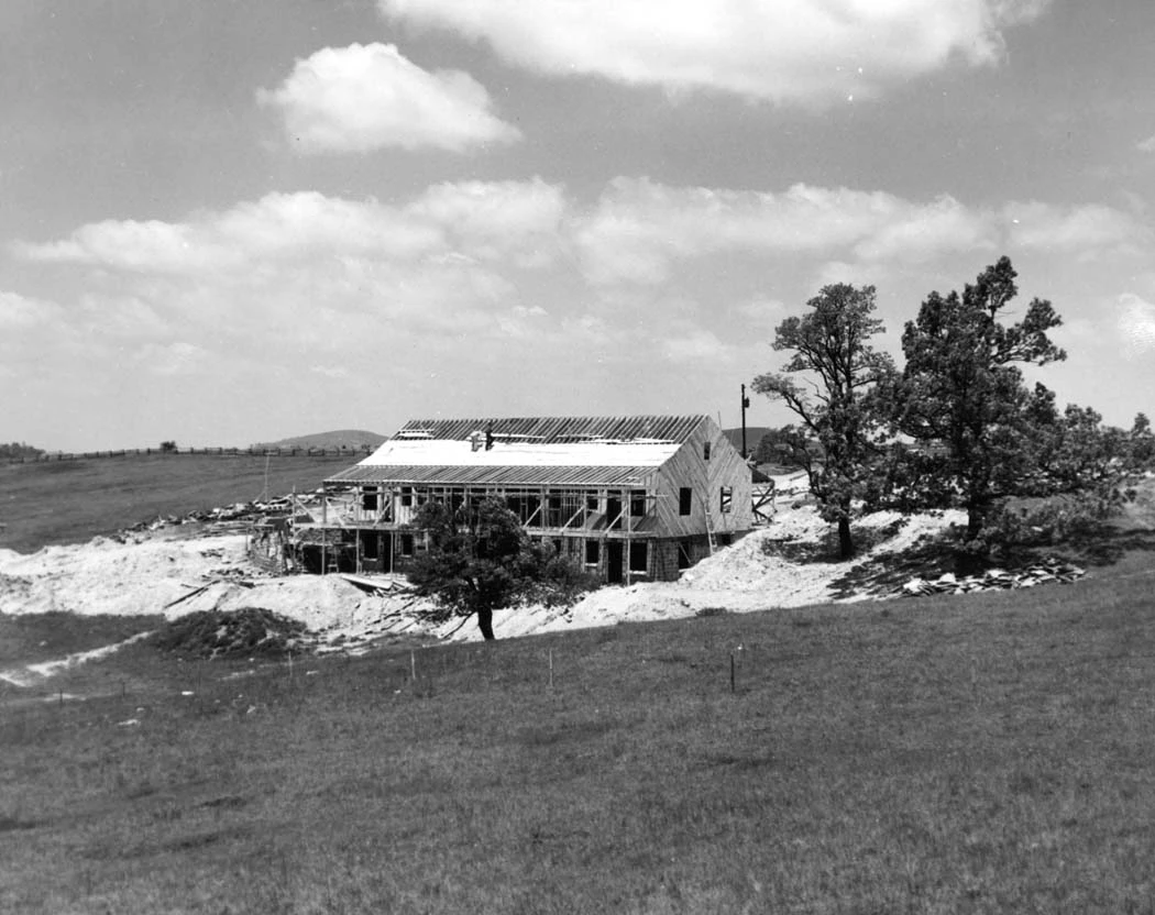 Bluffs Lodge under construction, 1949 Several pine trees grow beside a construction site where a two-story lodge is being built