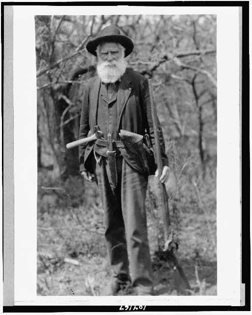 Black and white image of Daniel Freeman with a white beard, brimmed hat, and tools