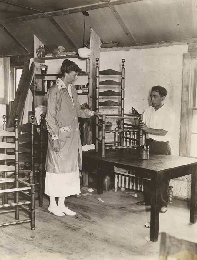 Eleanor Roosevelt and Matthew Famiglietti stand by a wooden chair atop a table, with more chairs in the background