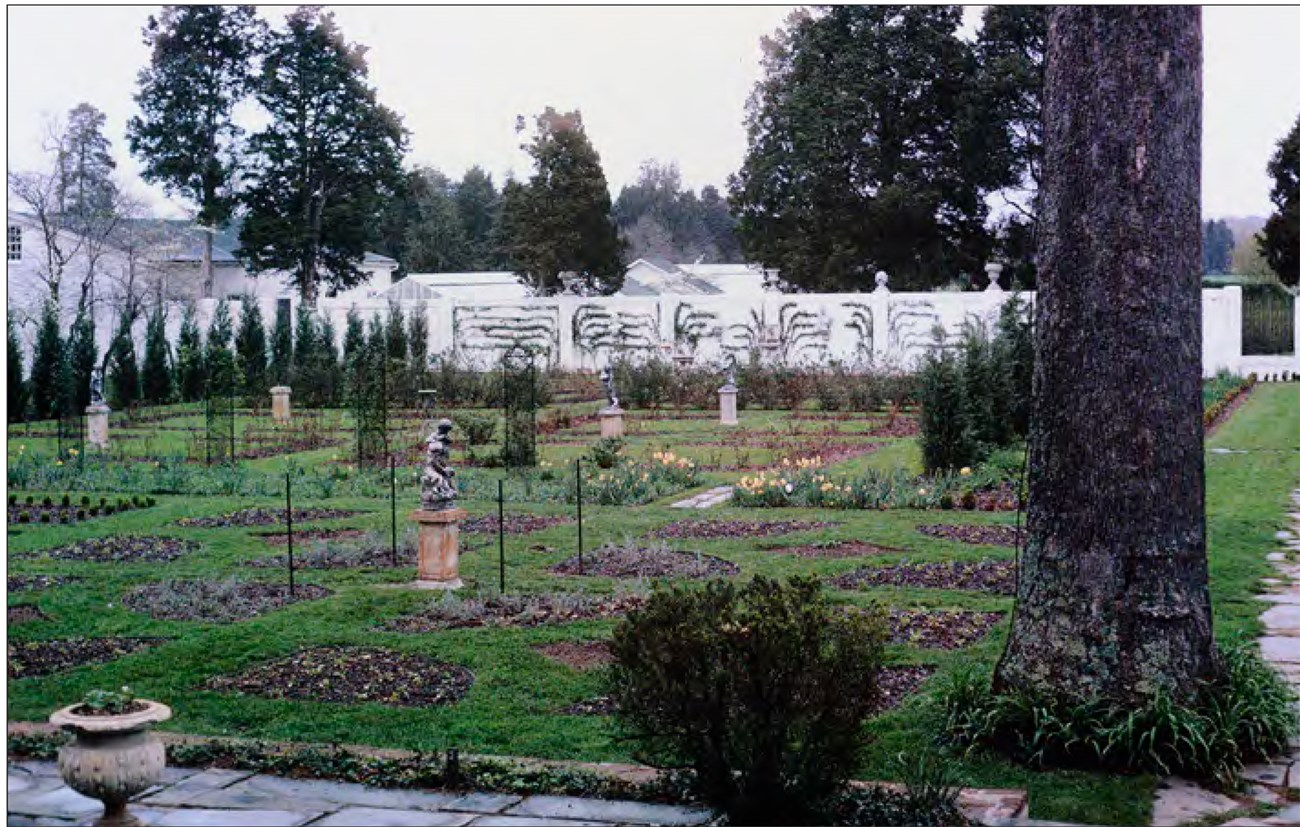 A wall and walkways form a perimeter around garden beds, with turf growing on the walkways between each bed.