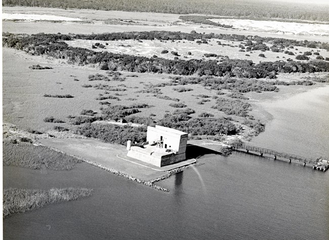 Aerial view of stone fortification at the edge of a river, near a dock and undeveloped area