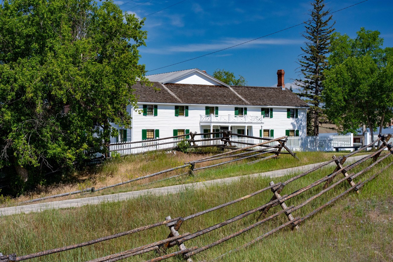 The Grant‐Kohrs House A grand white house stands in the center of complex of ranch buildings against the backdrop of the Montana sky.