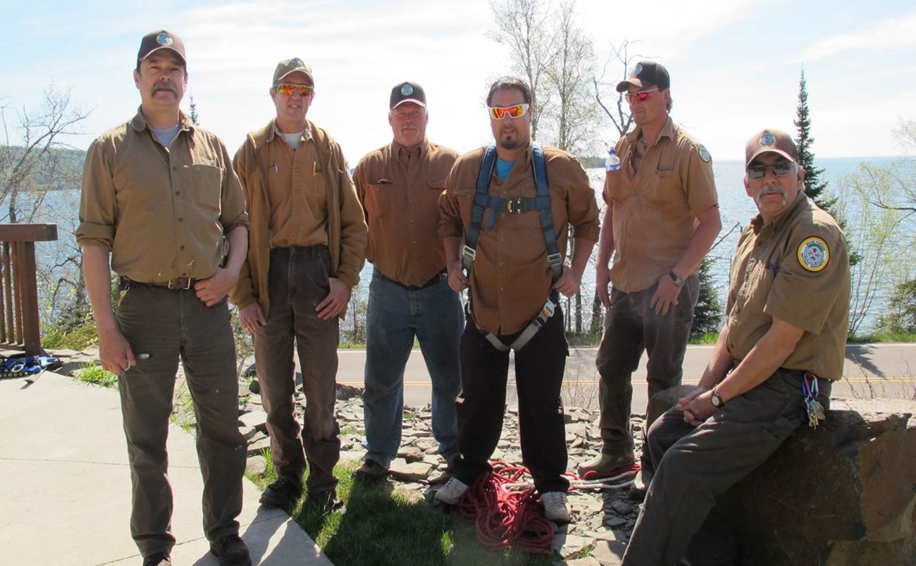 Six crew members pose with a lake in the background as they prepare for training