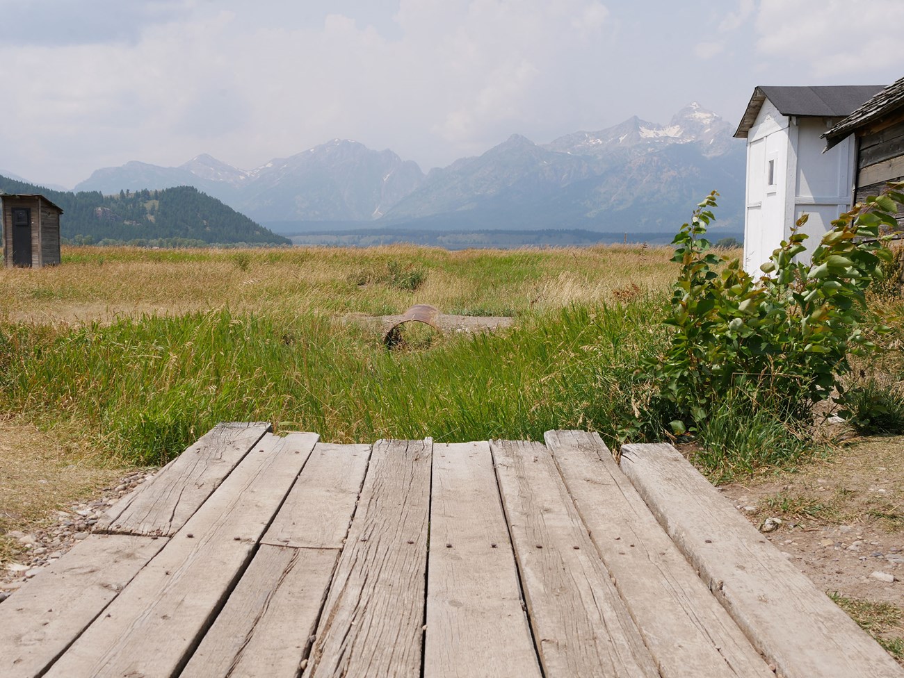 GRTE_MormonRow A wooden footbridge spans an irrigation ditch in a grassy field, with mountains beyond