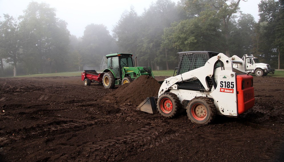 Preparing for the FDR Home Garden Restoration A heap of fine, dark topsoil stands in the middle of an expanse of dirt, with a backhoe and a tractor.