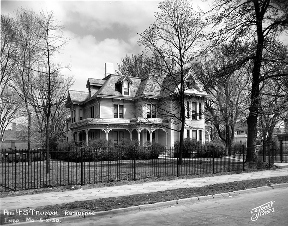Home of President Harry S. Truman in Independence, Missouri, May 2, 1950 Landscape features surrounding a Victorian house with a wrap around porch include foundation shrubs, trees in the lawn, and a perimeter fence.
