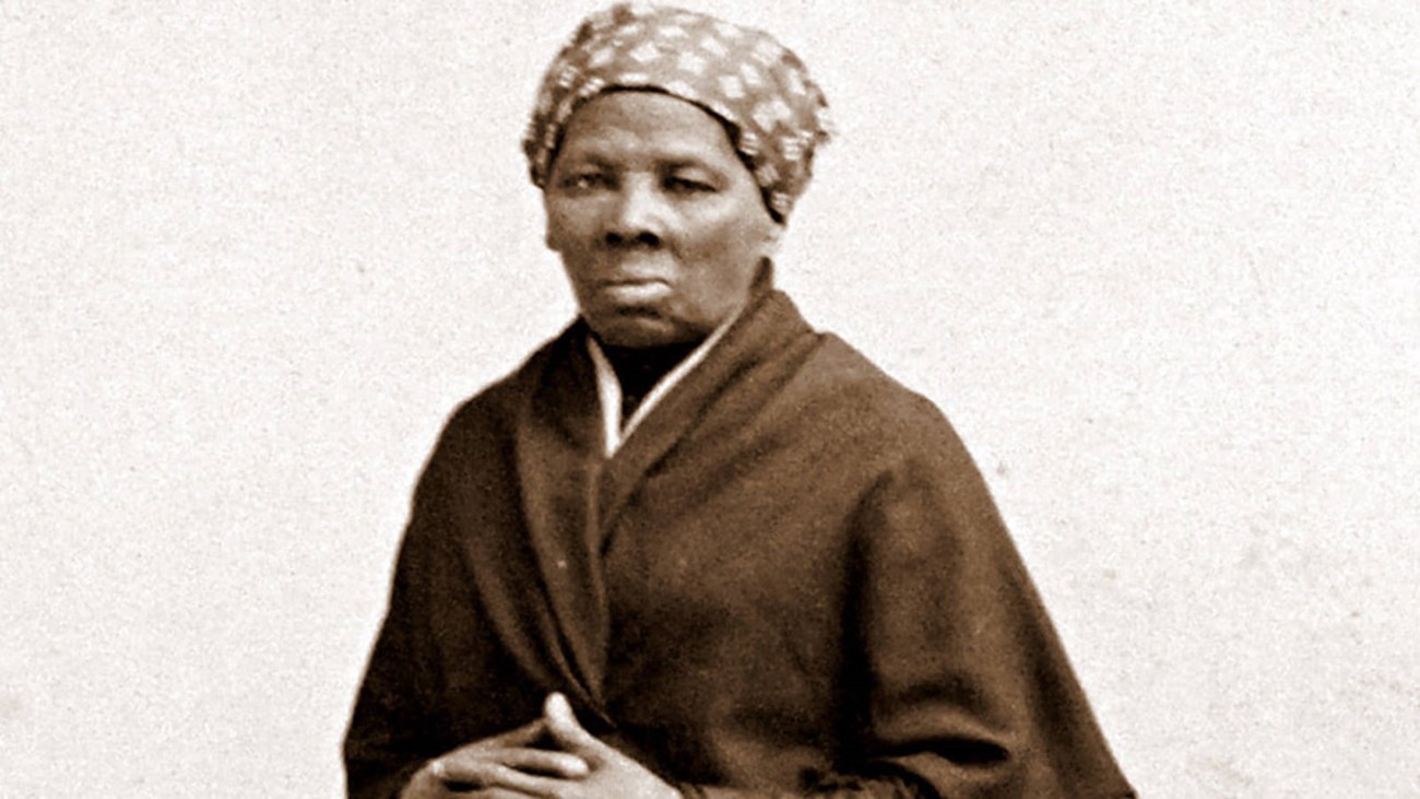 Portrait of an African American woman with a headscarf and cloak, her hands folded in front of her.