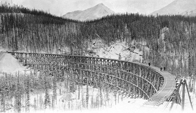 Copper River and Northwestern Railroad - large Tiny figures stand on the curve of a long wooden railroad bridge