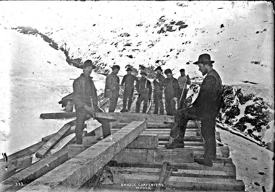 A group of 8 men pause on a partially-completed railway through a winter landscape.