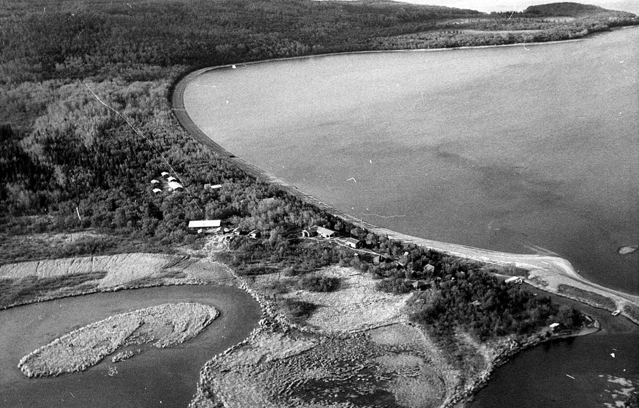 KATM Brooks Camp aerial, 1965 Black and white aerial photo of camp development near a curving shoreline, where a river meets a lake.