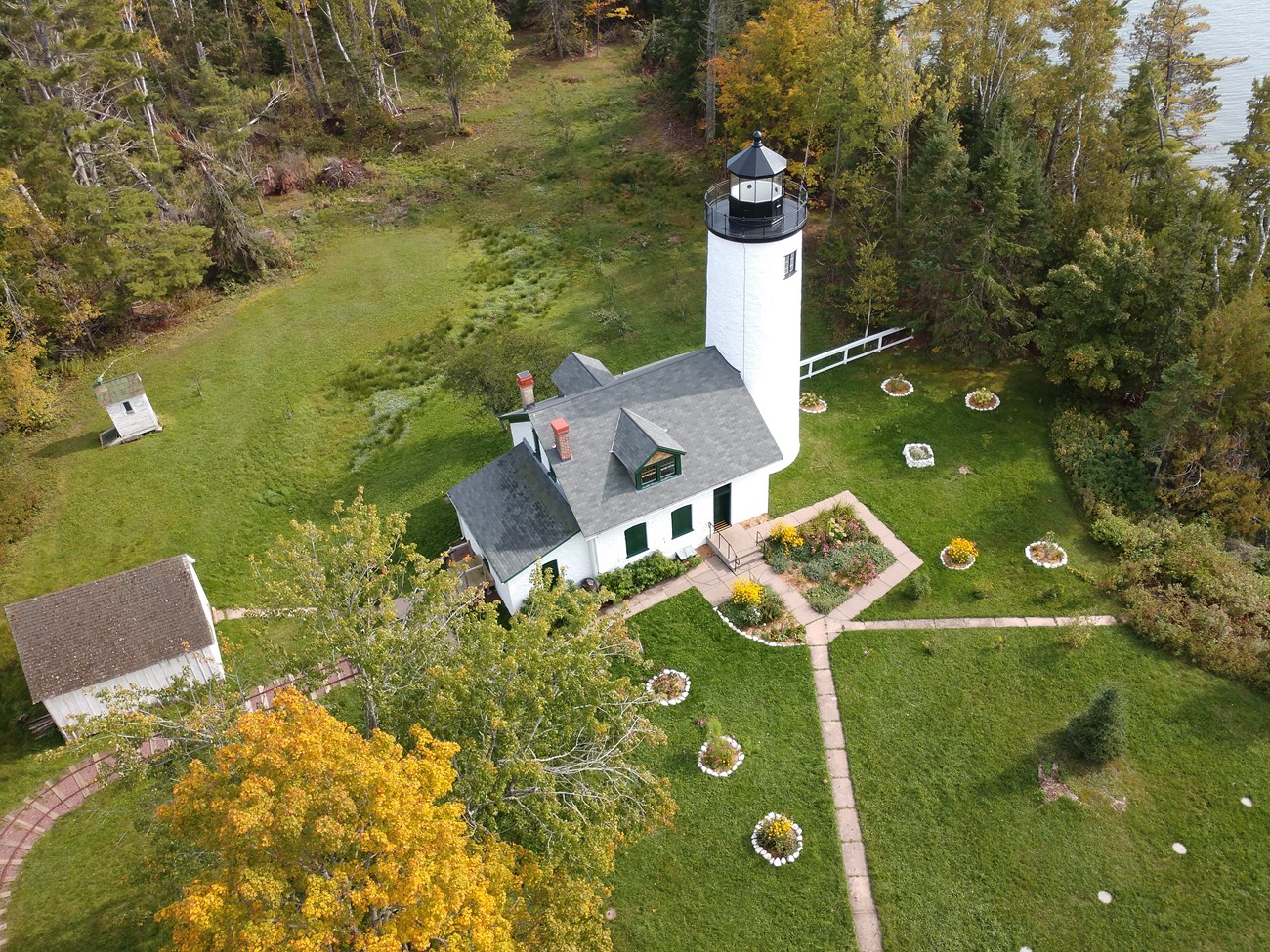 Overhead view of the old Michigan Lighthouse landscape, with tram tracks leading in from the left, walkways and gardens, and a perimeter of trees