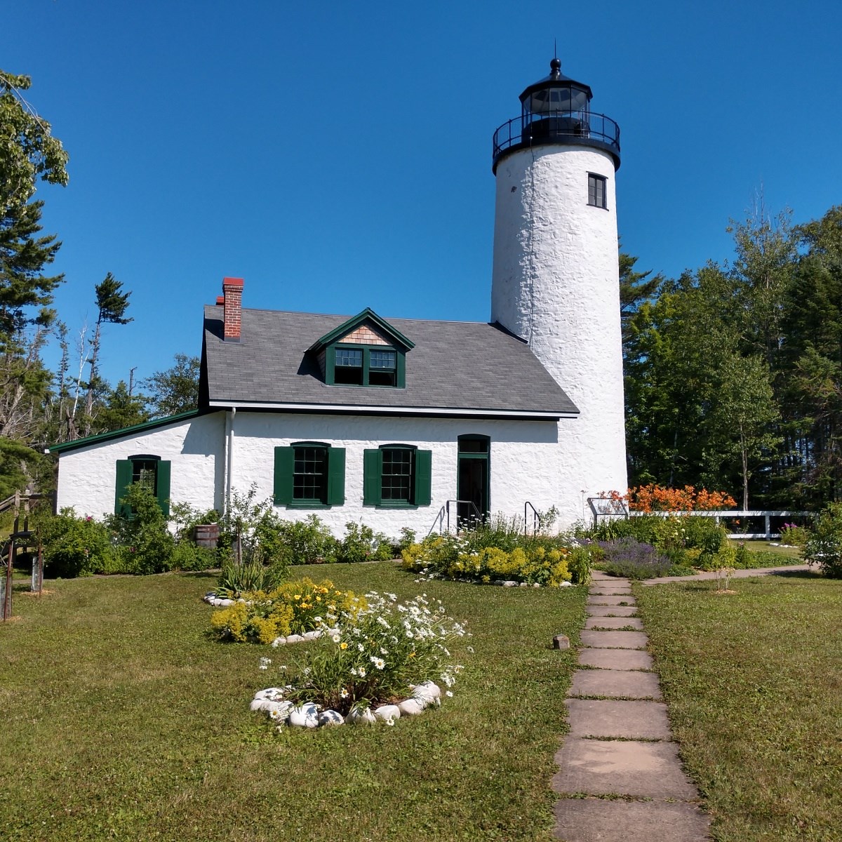 A walkway leads to a short lighthouse, with garden beds in front