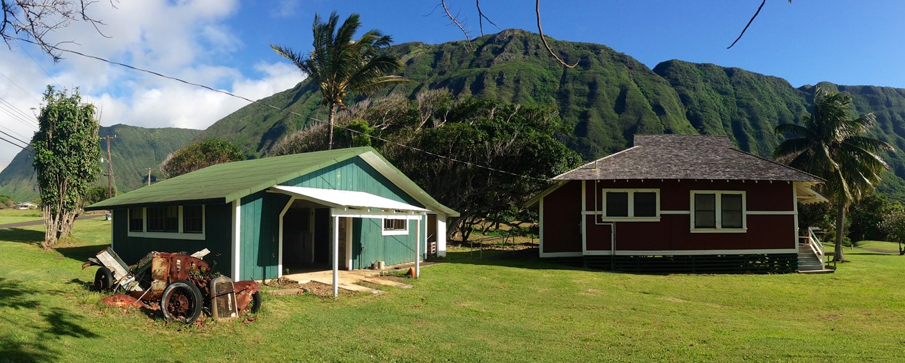 Two single-story structures surrounded by lawn, with tall cliffs in the background