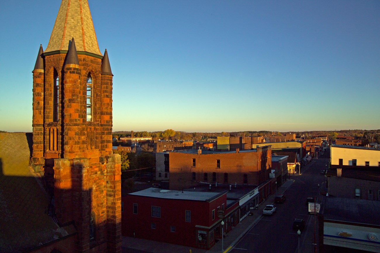 Morning light illuminates the stones of the steeple of St. Anne's and Calumet's commercial district of low brick buildings.
