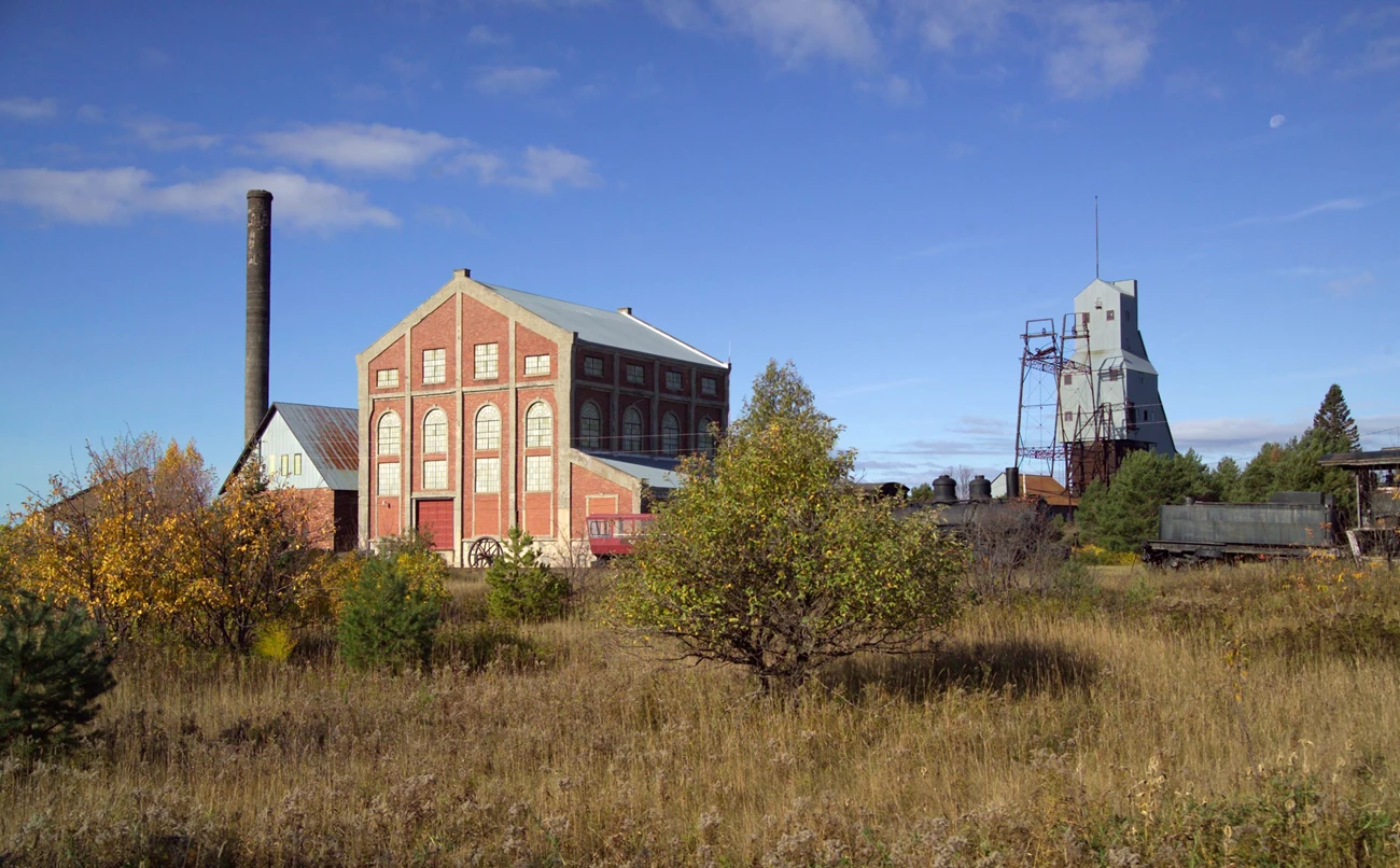 Quincy Mine Hoist Association Property within the Quincy Unit of Keweenaw National Historical Park Tall industrial structures, including a brick building, tower, and hoist, surrounded by a landscape of low trees and grass in fall colors