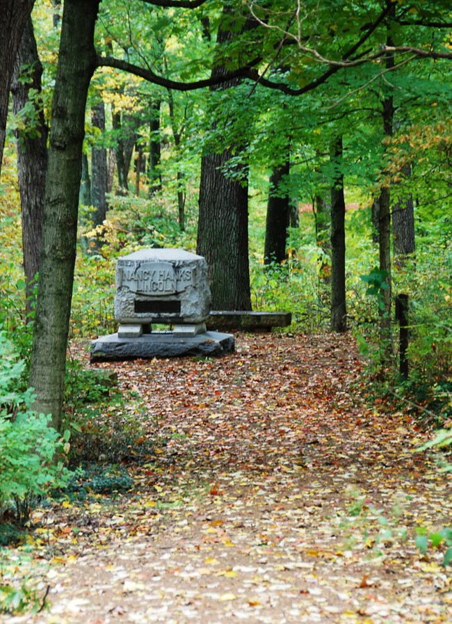 Trail of Twelve Stones A rectangular stone monument at the end of a trail scattered with leaves, under a canopy of leafy trees