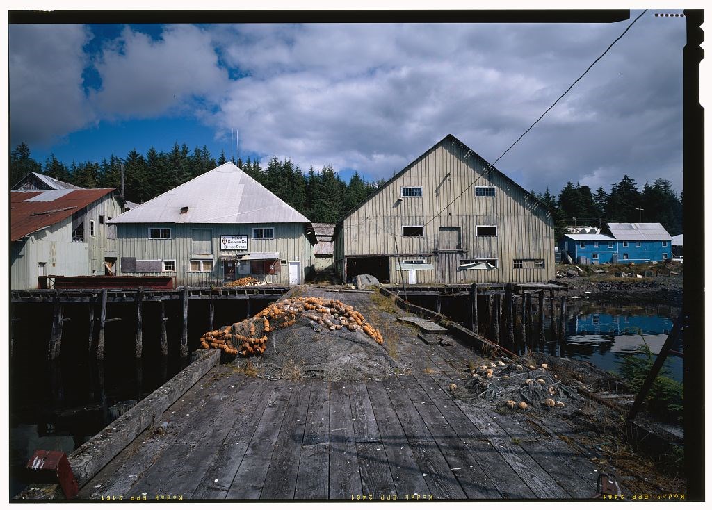 View of cannery buildings on wooden piers from the dock over the water.