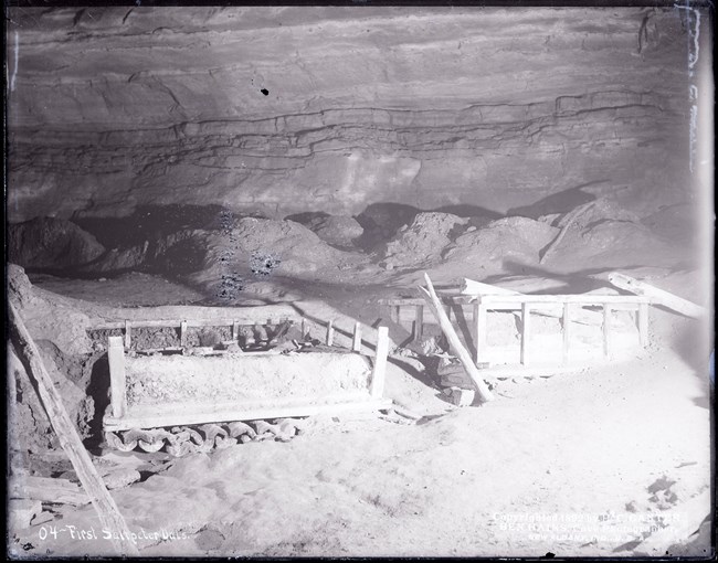 Two square vats formed by broken wooden frames in the interior floor of a cave