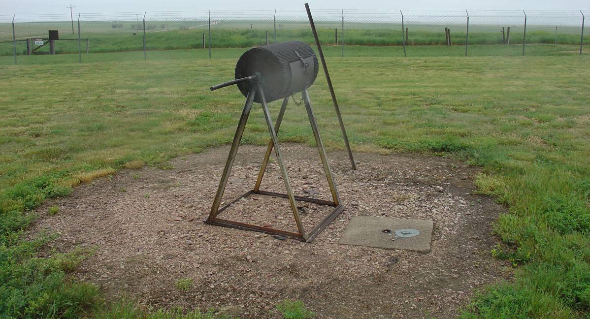The code burner is a cylindrical device on a triangular base, surrounded by open lawn.