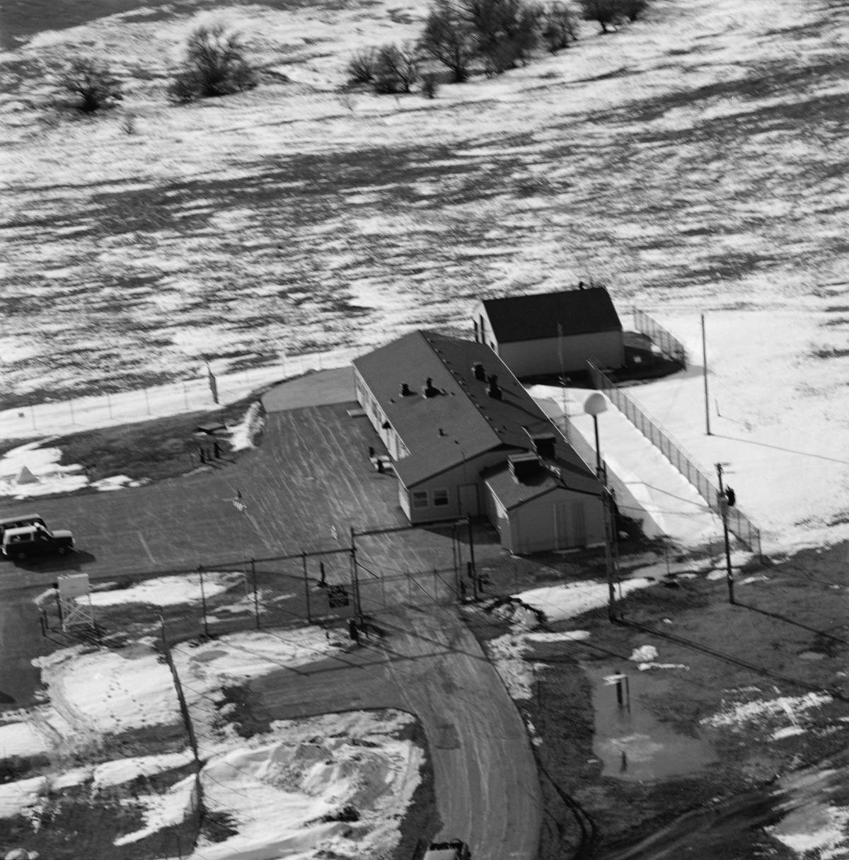 MIMI overhead Aerial view of Delta-01 with road leading to building cluster, surrounded by open snowy fields.