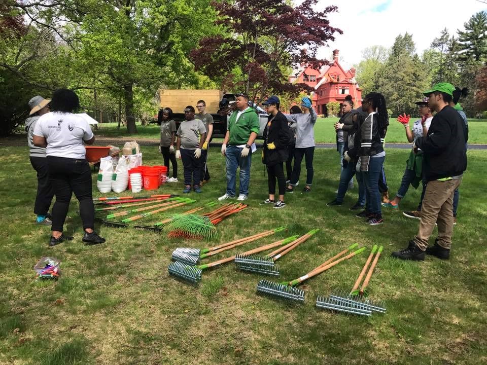 Tools lie on the ground in front of a group of students with gloves, in front of Glenmont