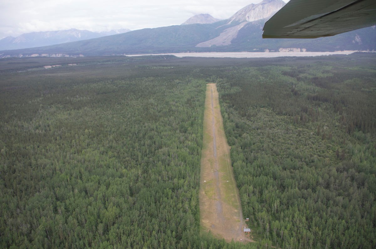 Dirt and grass landing strip seen from the air, surrounded by thick green forest