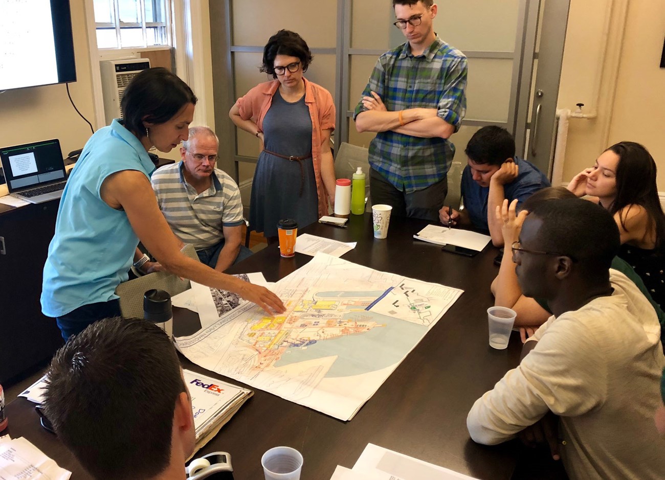 Navy-Yard-Charette_Designing-the-Parks_crop A group of people is gathered around a wooden table, looking on as one person points to a site plan.