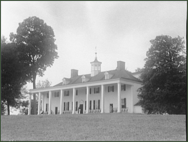 lt= Pillars line the front of a long, two-story white house.