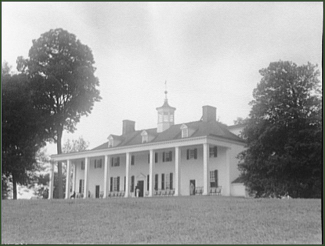 Pillars line the front of a long, two-story white house.