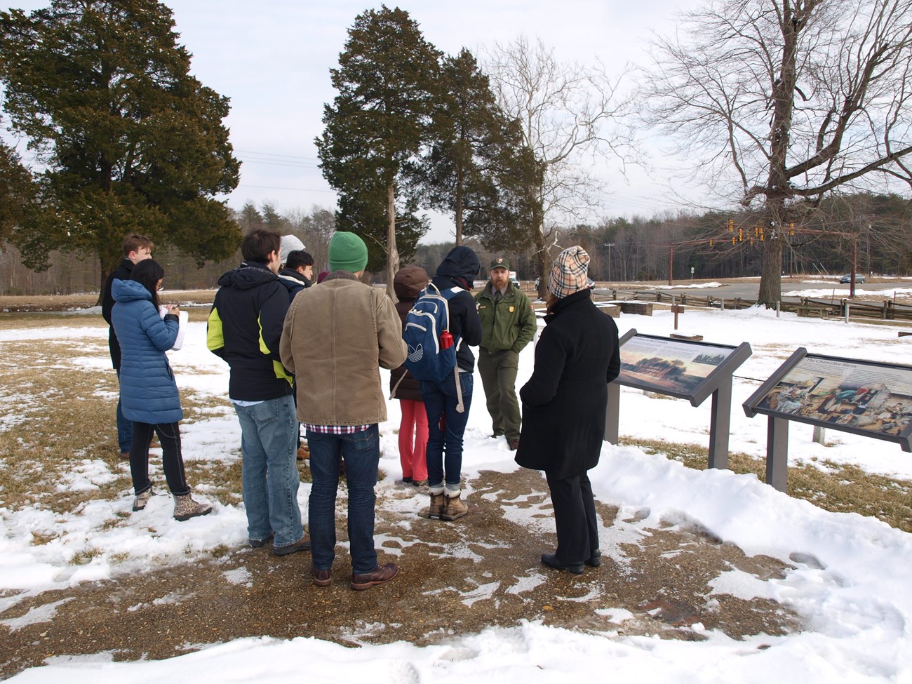 A man in NPS uniform talks to a small group, standing on patches of snow
