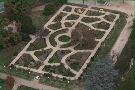 An aerial view shows symmetrical curving pathways dividing garden beds.
