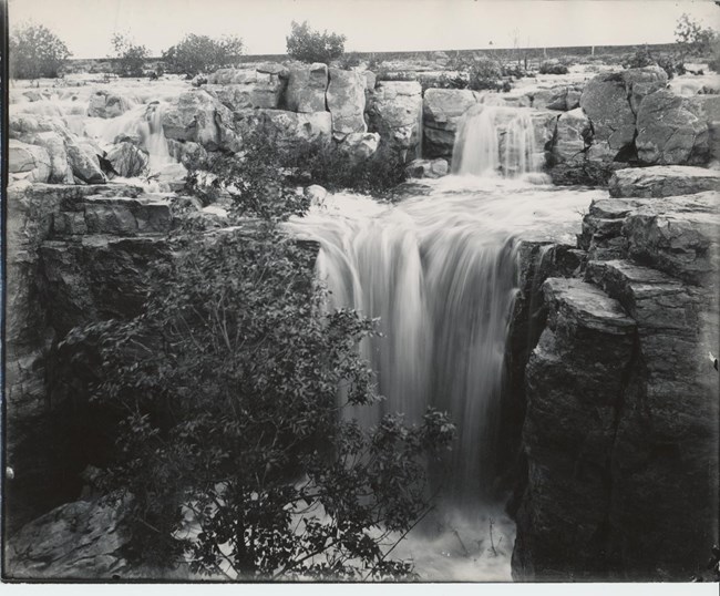 Black and white photo of wide, rushing waterfall with little smaller falls above it