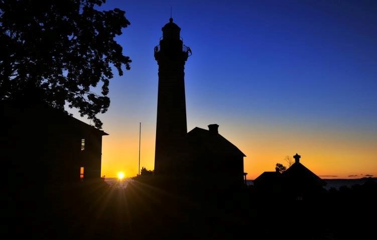 Sunrise begins behind the silhouette of a lighthouse