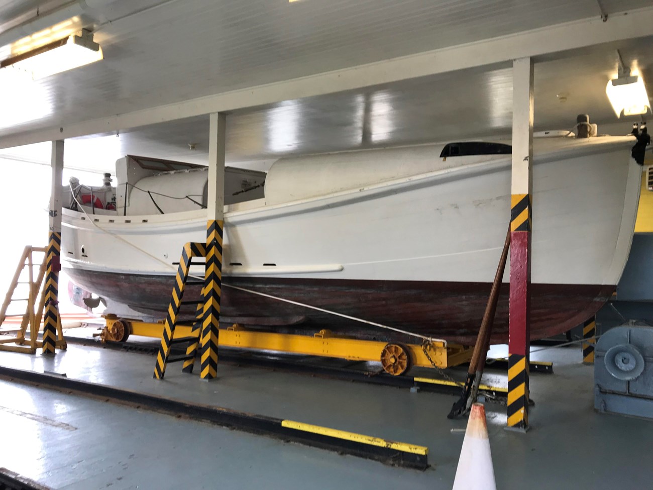 The restored 36-foot Motorized Lifeboat CG-36542 within the Point Reyes Lifeboat Station's boathouse in 2019. A color photograph of an old, 36-foot-long, motorized lifeboat resting on a rail car on tracks within the boat bay of boathouse. The lifeboat is painted white above the waterline and brick red below.