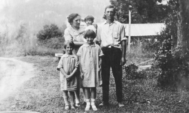 Two adults and three young girls pose for a photo, standing in an outdoor yard in 1927.