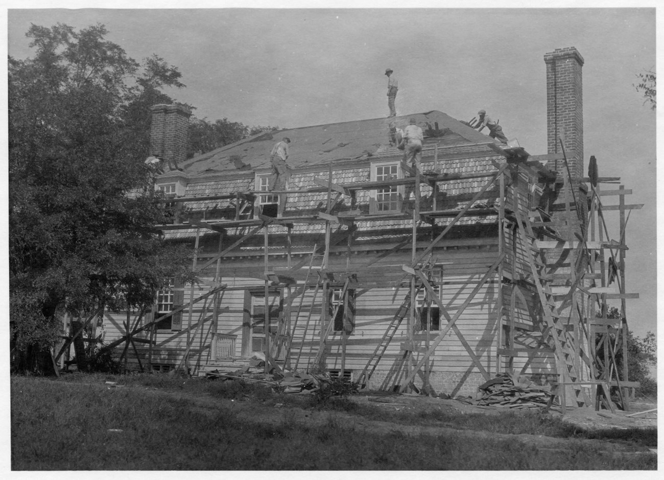 People work on different areas of a house that is covered with wooden scaffolding