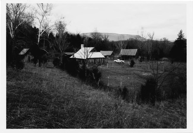 View over rolling terrain towards a farmstead, a cluster of wooden structures