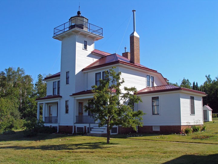 A fruit tree, gardens, and lawn surround a two story structure with a light tower built into it.