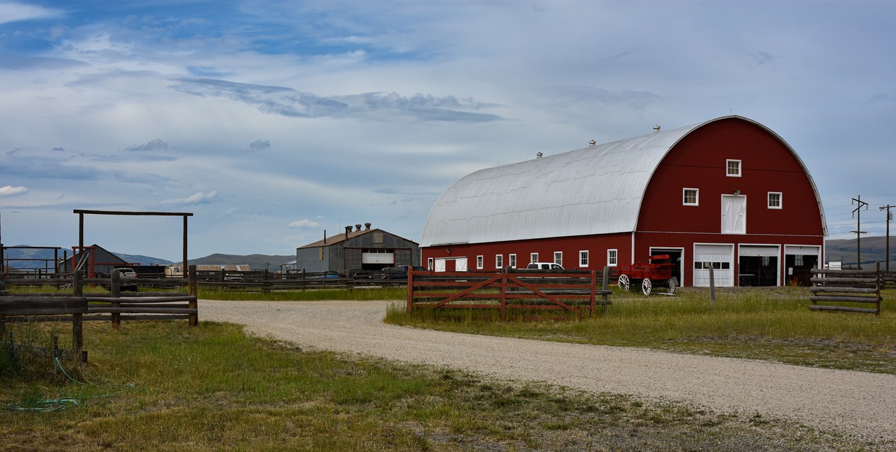 A large red barn with rounded roof and several metal accessory buildings stand against a bright blue sky