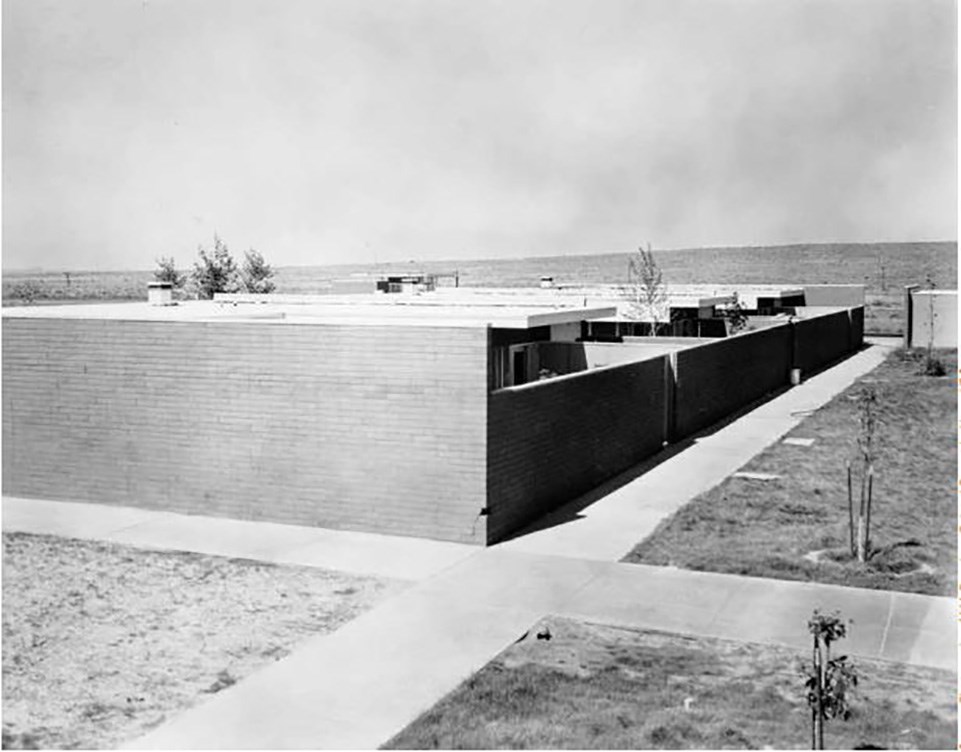 Sidewalks cross at the corner of a row of residences at the Painted Desert Community Complex, with courtyards behind a brick wall.