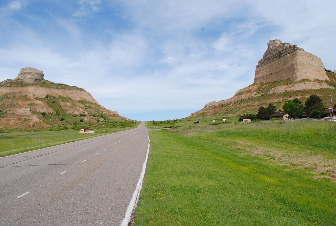 A straigt road passes through a pass between the steep rocky formations of Scotts Bluff.