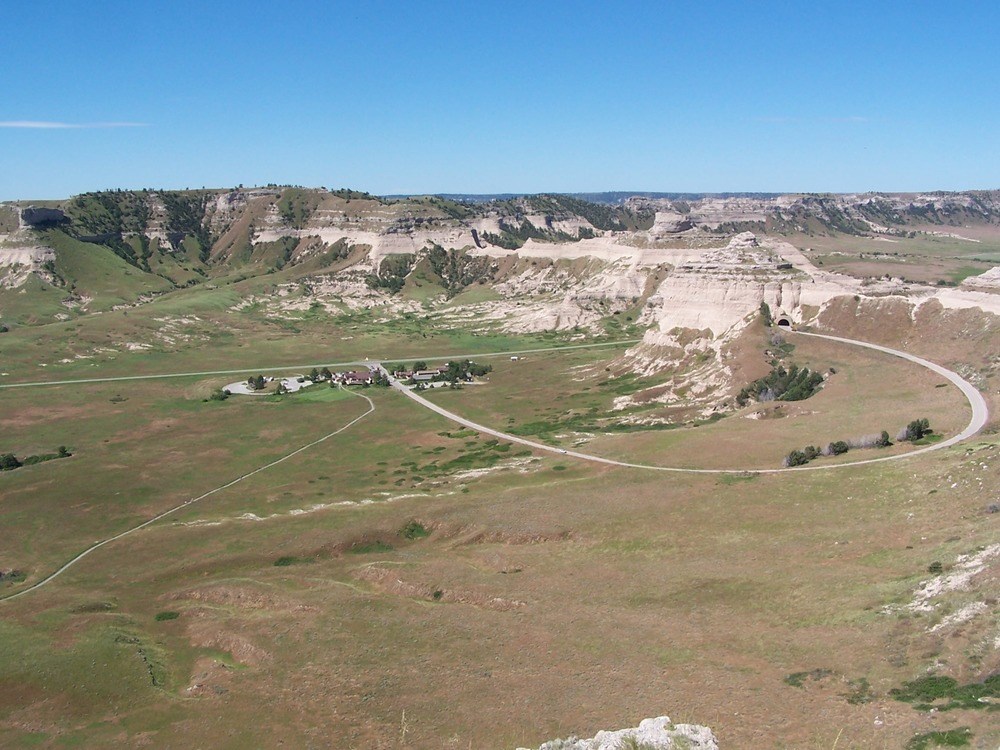 SCBL-Overlookview A view of the Scotts Bluff landscape from an overlook includes the Main Complex buildings, rocky bluff, and curving road.