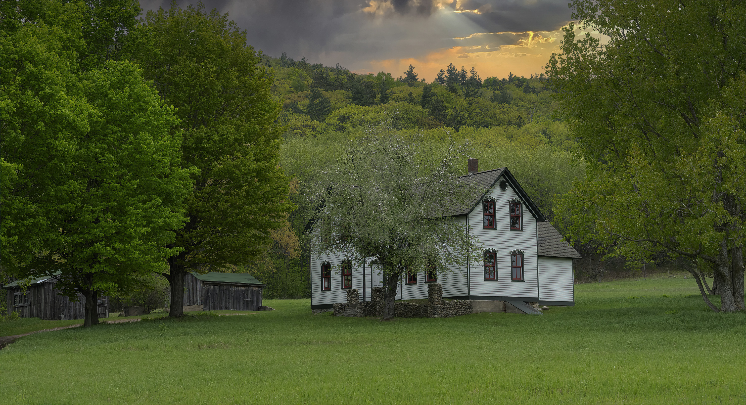 A cloudy sky glows over a farm, with a two-story farm house, tall apple tree, and outbuildings