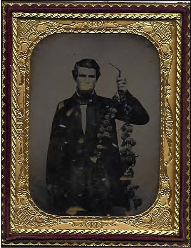 Historic photo of a man, Levi Tower, in an ornate frame. He holds up a branch of peaches.